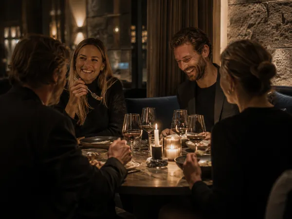 Weniger Inszenierung, mehr Gefühl – Genuss, der nach Berg und Tal schmeckt. Vier Personen genießen ein Abendessen bei Kerzenlicht in einem Restaurant