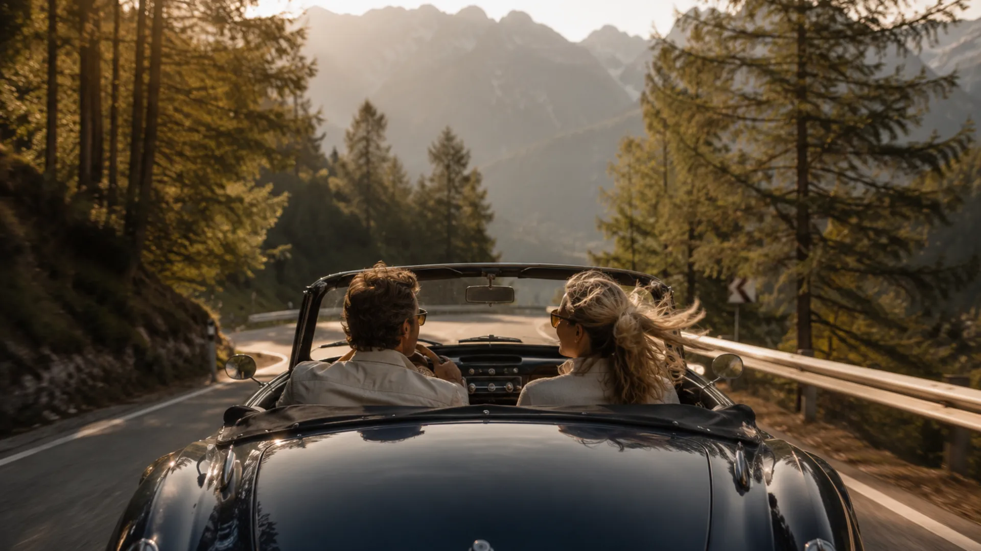 Paar fährt im Cabriolet durch eine kurvenreiche Bergstraße im Wald