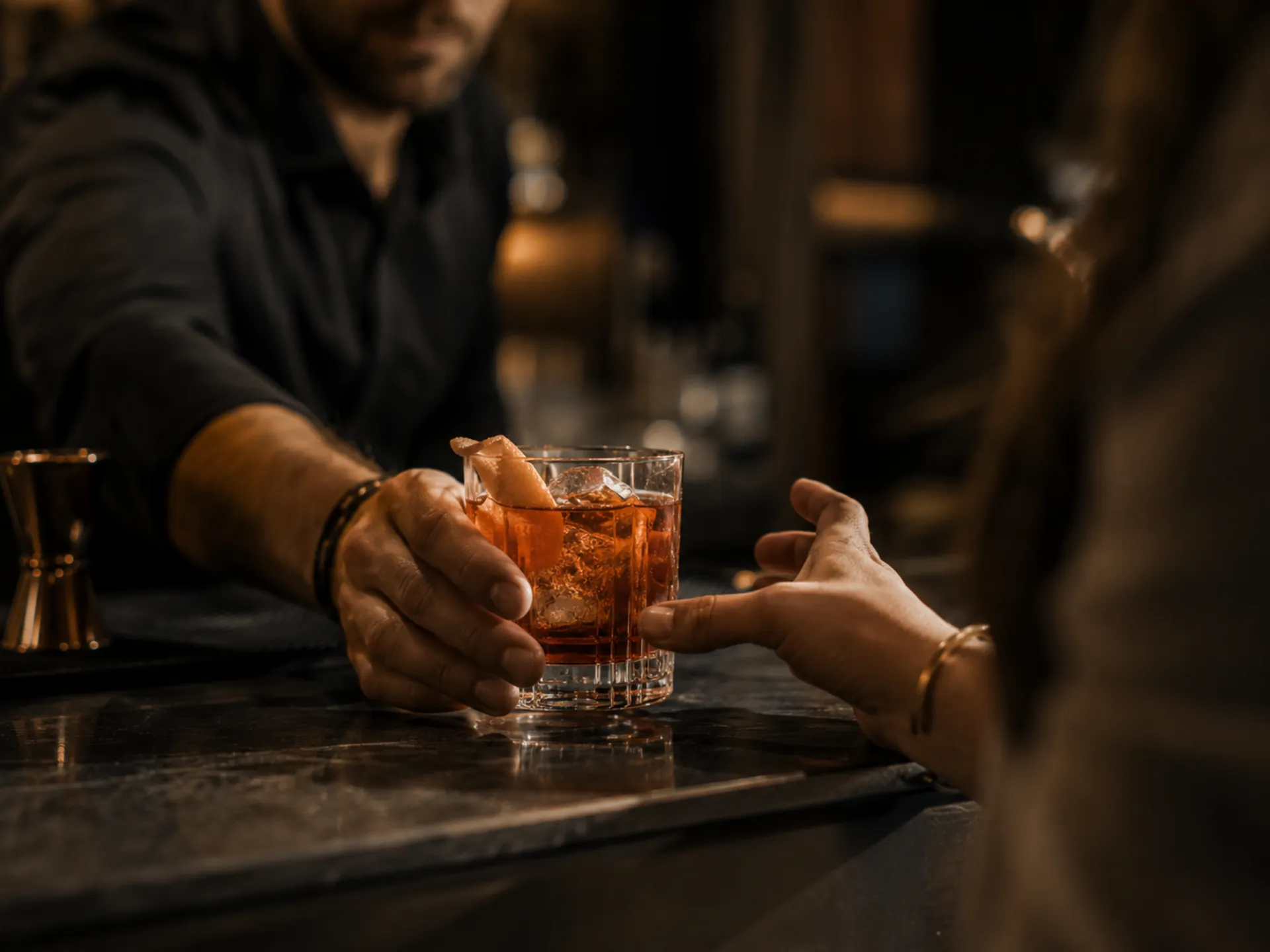 Barkeeper reicht ein Glas mit bernsteinfarbenem Cocktail und Orangenschale